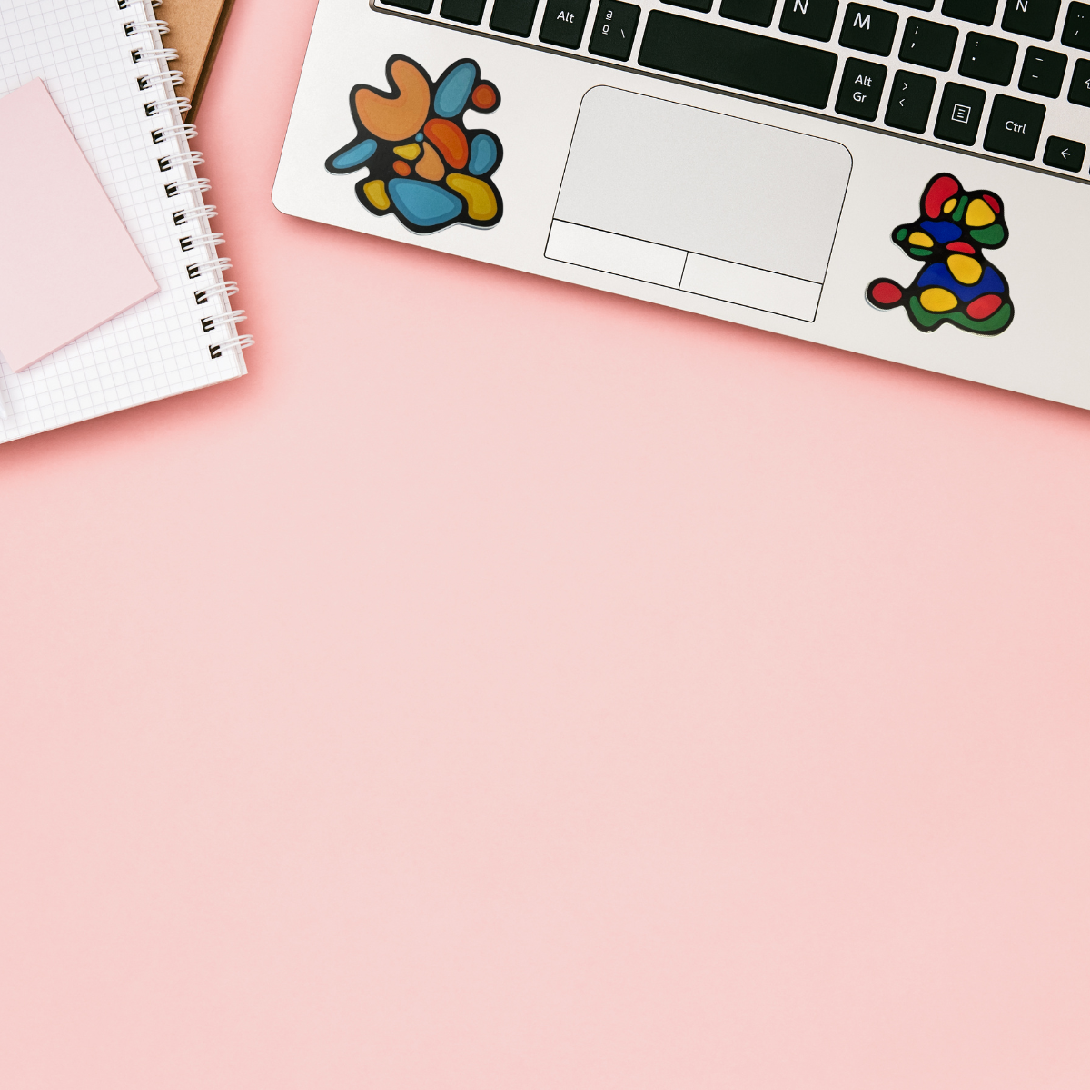 A small abstract mouse-shaped sticker or decal with a black outline and colorful filled spots in red, yellow, green, and blue, placed on a plain light background.
