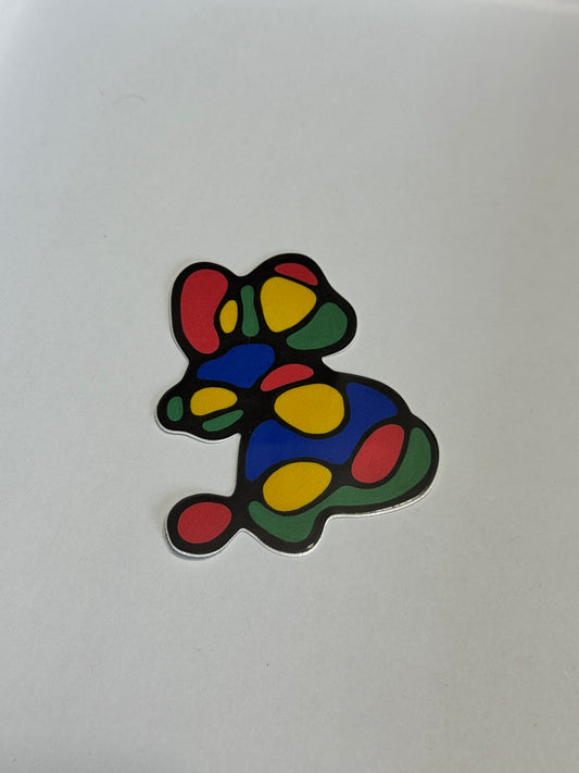 A small abstract mouse-shaped sticker or decal with a black outline and colorful filled spots in red, yellow, green, and blue, placed on a plain light background.